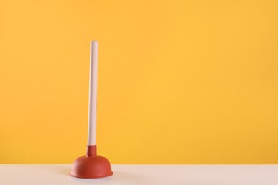 Photo of Plunger on white table against yellow background. Space for text