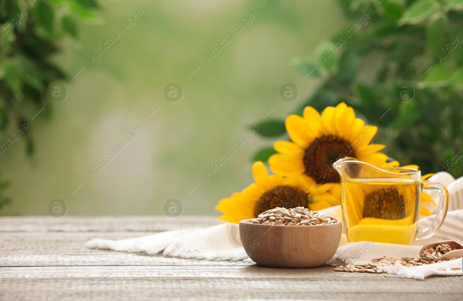 Photo of Sunflower oil and seeds on wooden table against blurred background, space for text