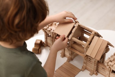 Little boy playing with wooden entry gate at white table in room, closeup. Child's toy