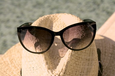 Stylish hat and sunglasses on blurred background, closeup