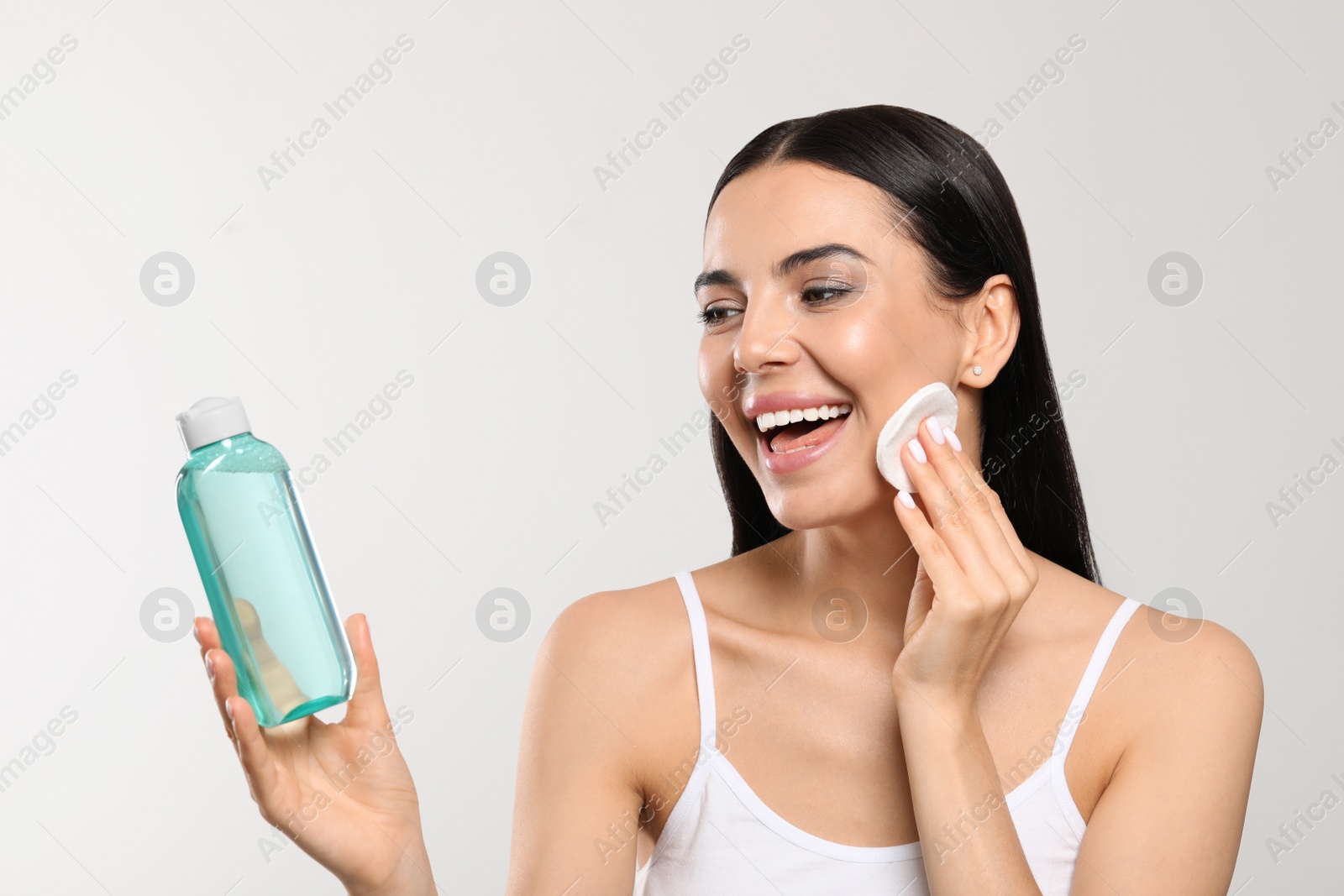 Photo of Young woman using cotton pad with micellar water on light grey background