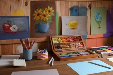 Photo of Blank sheets of paper, colorful chalk pastels and drawing pencils on wooden table indoors. Modern artist's workplace