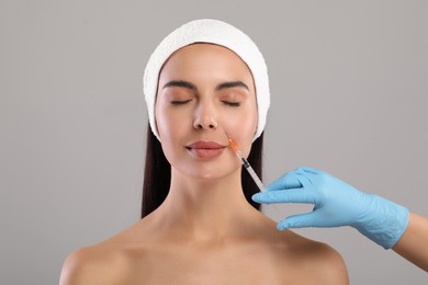 Photo of Doctor giving facial injection to young woman on light grey background. Cosmetic surgery