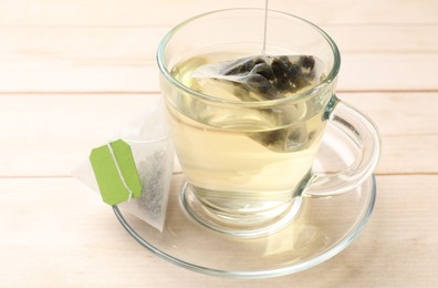 Photo of Putting tea bag in glass cup on light wooden table, closeup