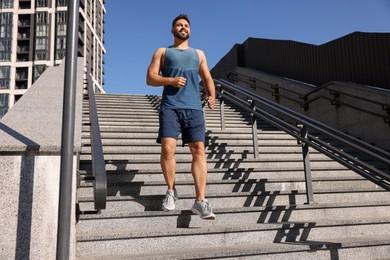 Photo of Happy man running down stairs outdoors on sunny day. Space for text
