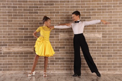 Beautifully dressed couple of kids dancing together near brick wall indoors