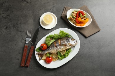Delicious roasted fish with lemon on dark grey table, flat lay