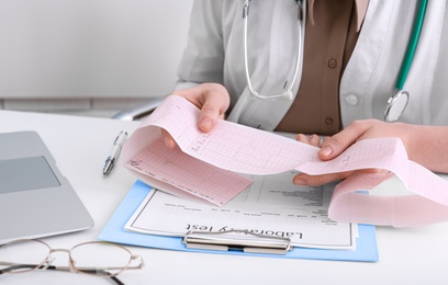 Photo of Doctor examining cardiogram at table in clinic, closeup