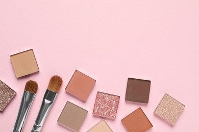 Photo of Different beautiful eye shadows and makeup brushes on pink background, flat lay. Space for text