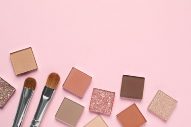 Different beautiful eye shadows and makeup brushes on pink background, flat lay. Space for text