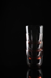 Photo of Stack of empty colorful whiskey glasses on black background, space for text