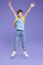 Photo of Back to school. Cute boy with backpack jumping on violet background