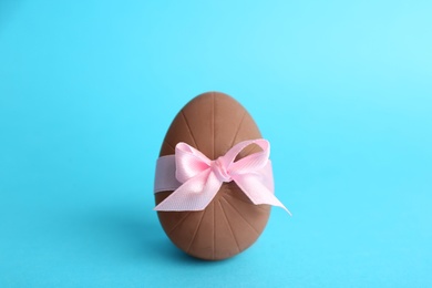 Sweet chocolate egg with pink bow on light blue background