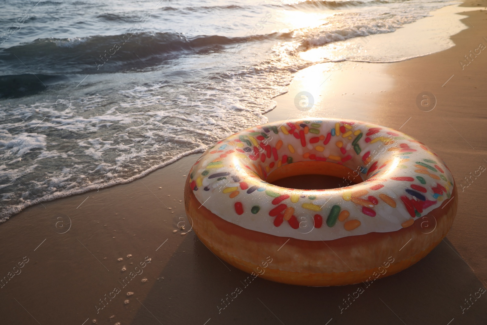 Photo of Inflatable ring with doughnut pattern on sunlit sandy beach near sea, space for text