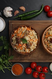 Photo of Delicious pilaf in bowls and products on black table, flat lay