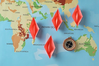 Photo of Bright paper boats and compass on world map, flat lay