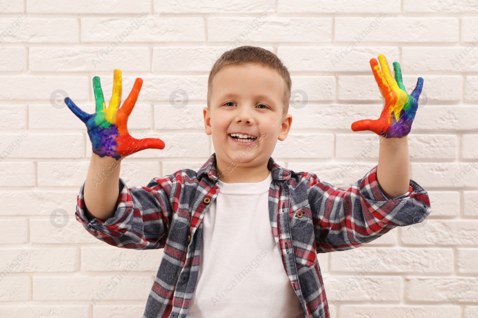 Photo of Happy little boy showing painted palms near white brick wall