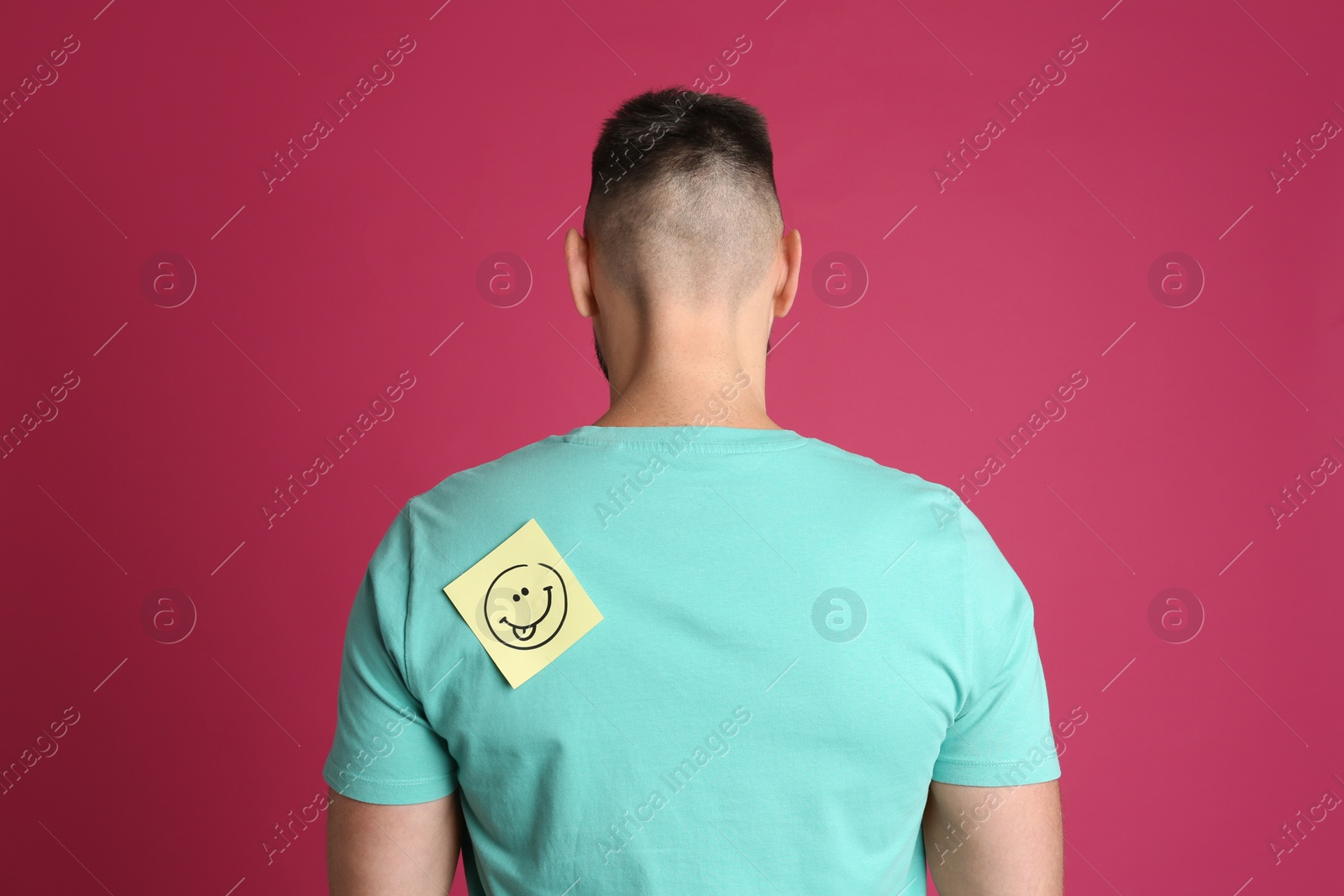 Photo of Man with smiling face sticker on back against pink background. April fool's day