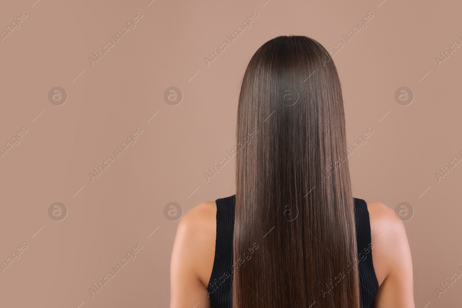 Photo of Hair styling. Woman with straight long hair on pale brown background, back view. Space for text