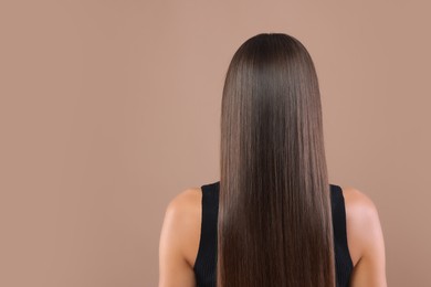 Hair styling. Woman with straight long hair on pale brown background, back view. Space for text