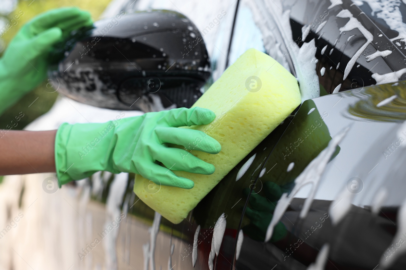 Photo of Woman washing car with sponge outdoors, closeup