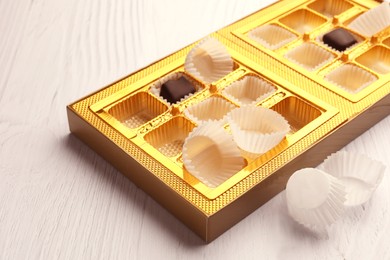 Photo of Partially empty box of chocolate candies on white wooden table