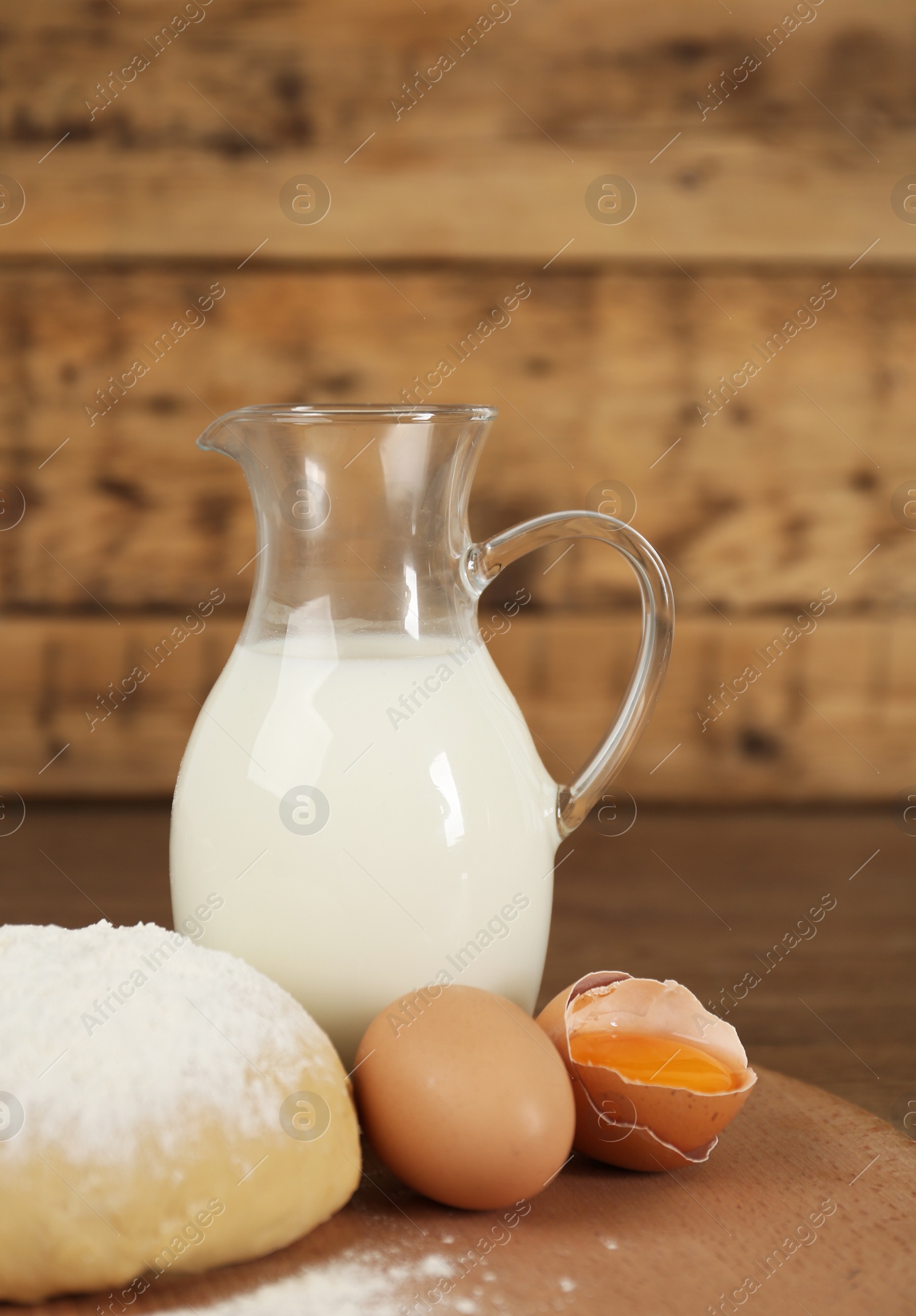 Photo of Raw eggs, dough and milk on wooden table. Baking pie