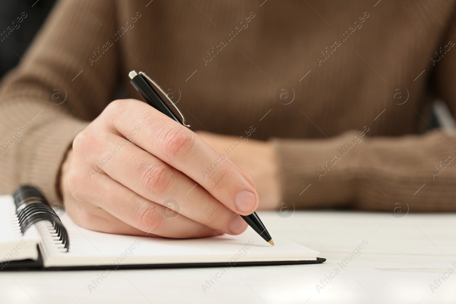 Photo of Man writing in notebook at white table, closeup. Space for text