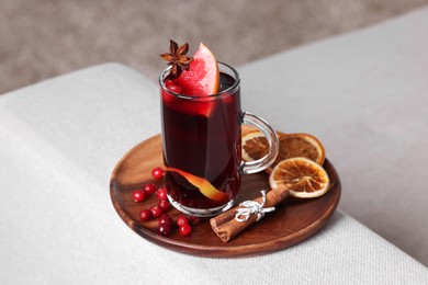 Photo of Aromatic mulled wine in cup and ingredients on sofa armrest