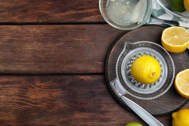 Photo of Glass squeezer and fresh lemons on wooden table, flat lay. Space for text
