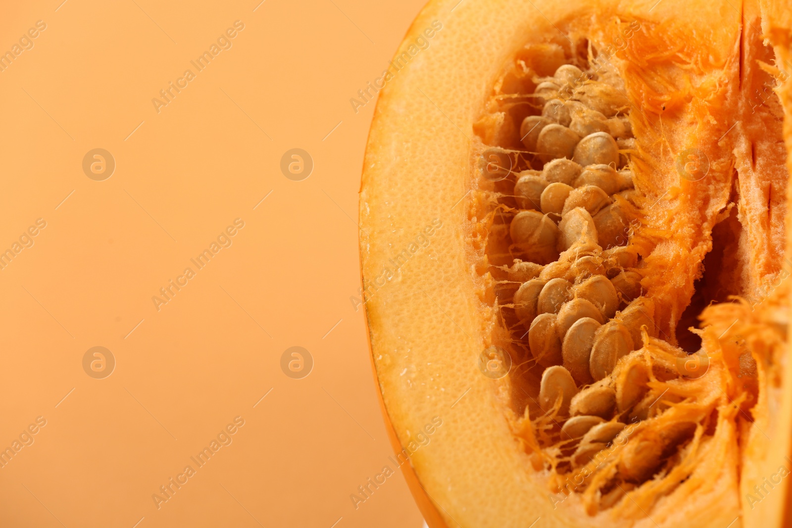 Photo of Cut fresh ripe pumpkin on pale orange background, closeup. Space for text