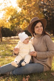 Photo of Happy mother with her baby daughter sitting on grass in autumn park