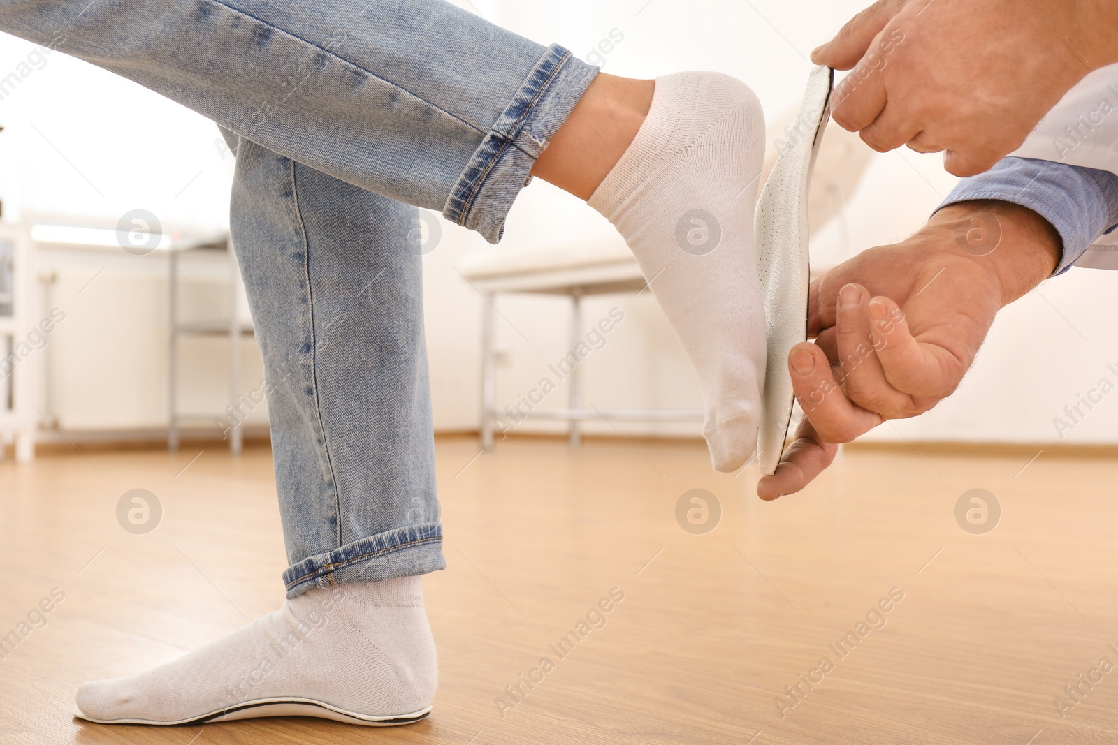 Photo of Male orthopedist fitting insole on patient's foot in clinic, closeup