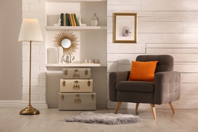Photo of Stylish room interior with comfortable armchair and storage trunks near white wall