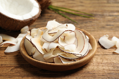 Delicious coconut chips in plate on wooden table