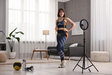 Photo of Happy sports blogger holding skipping rope while streaming online fitness lesson with smartphone at home