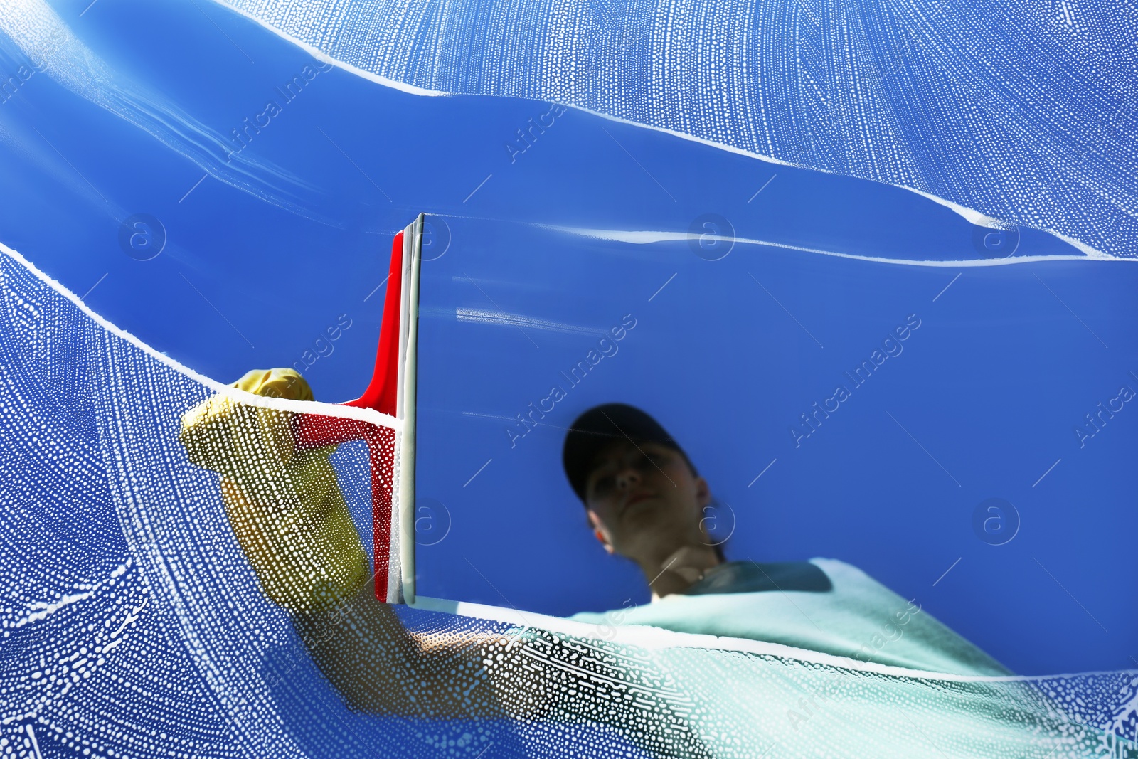 Photo of Woman cleaning glass with squeegee on sunny day