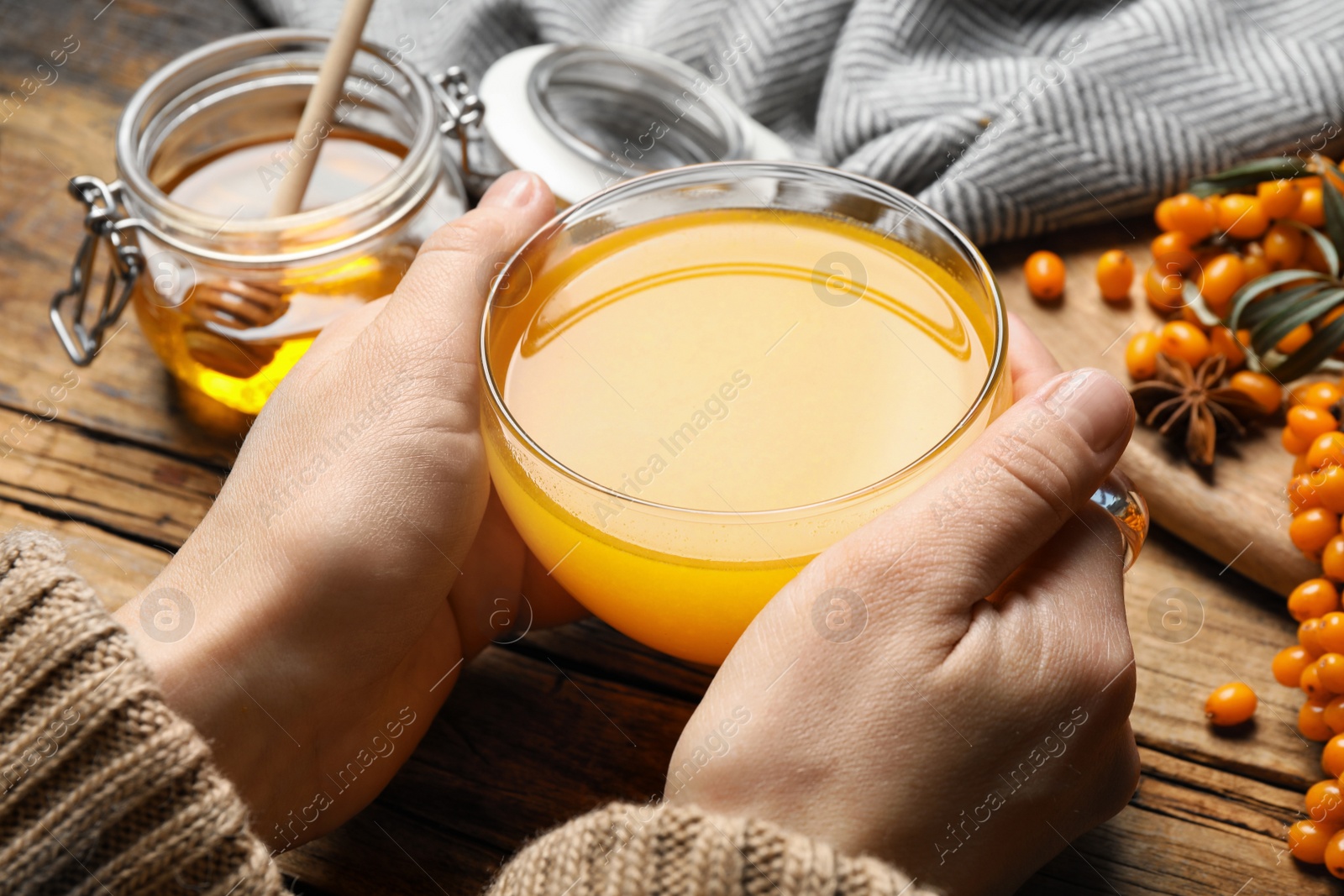 Photo of Woman with cup of fresh sea buckthorn tea at wooden table, closeup