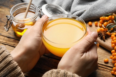 Photo of Woman with cup of fresh sea buckthorn tea at wooden table, closeup