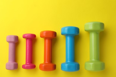 Photo of Many different stylish dumbbells on yellow background, flat lay