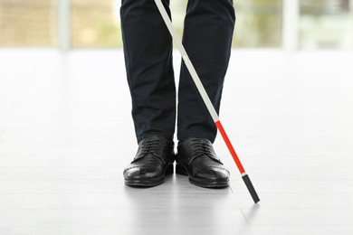 Photo of Blind person with long cane standing indoors, closeup