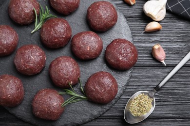 Photo of Many fresh raw meatballs and ingredients on black wooden table, flat lay