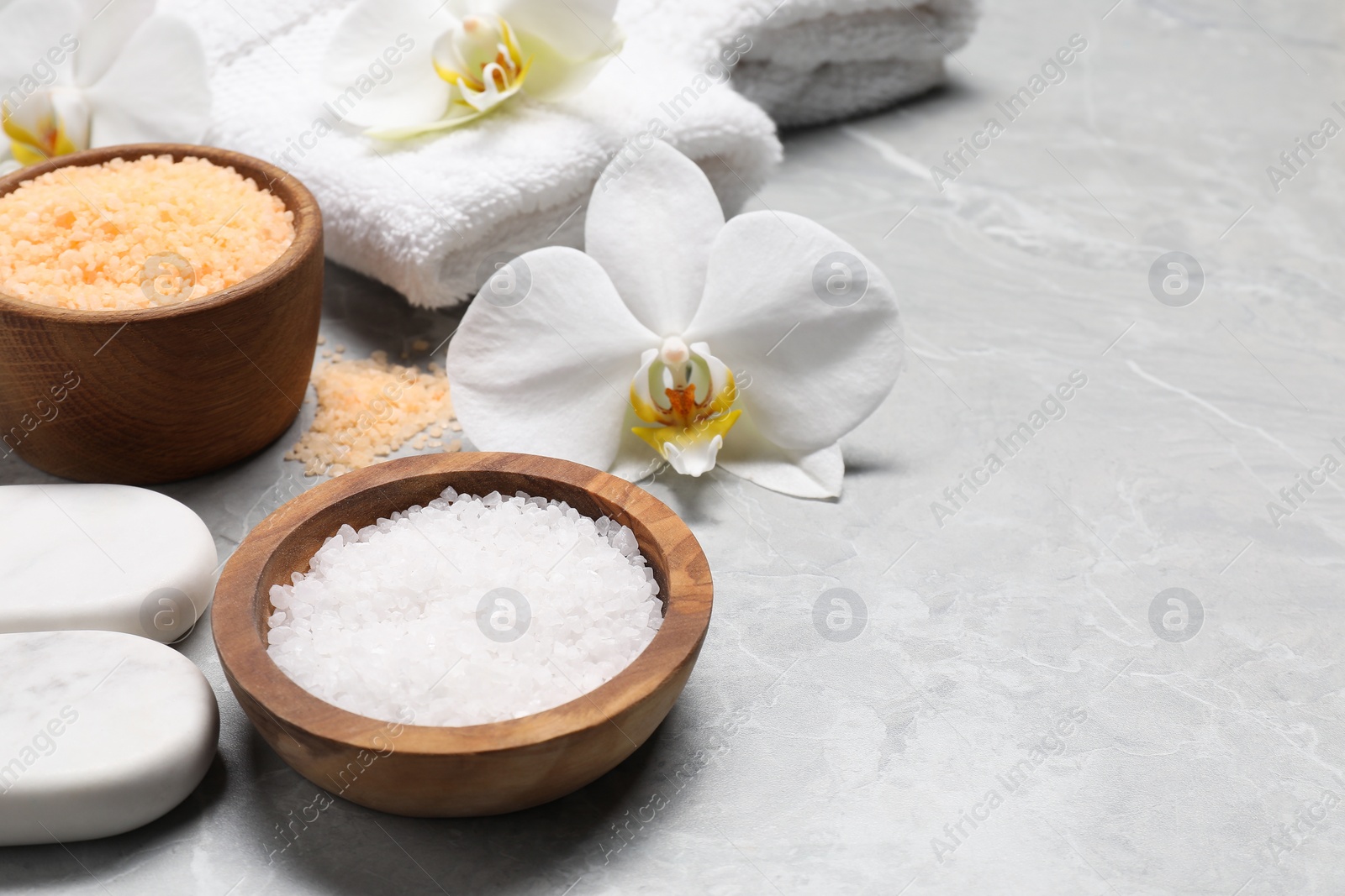 Photo of Natural sea salt in bowls, spa stones and flowers on grey marble table, space for text