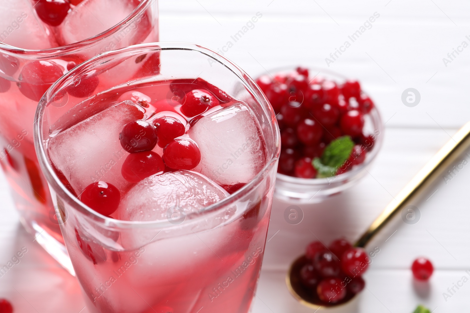 Photo of Tasty cranberry juice with ice cubes in glasses and fresh berries on white table, closeup. Space for text