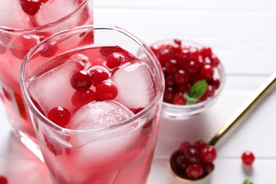 Photo of Tasty cranberry juice with ice cubes in glasses and fresh berries on white table, closeup. Space for text