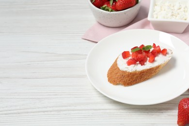 Photo of Delicious ricotta bruschetta with strawberry and mint on white wooden table. Space for text