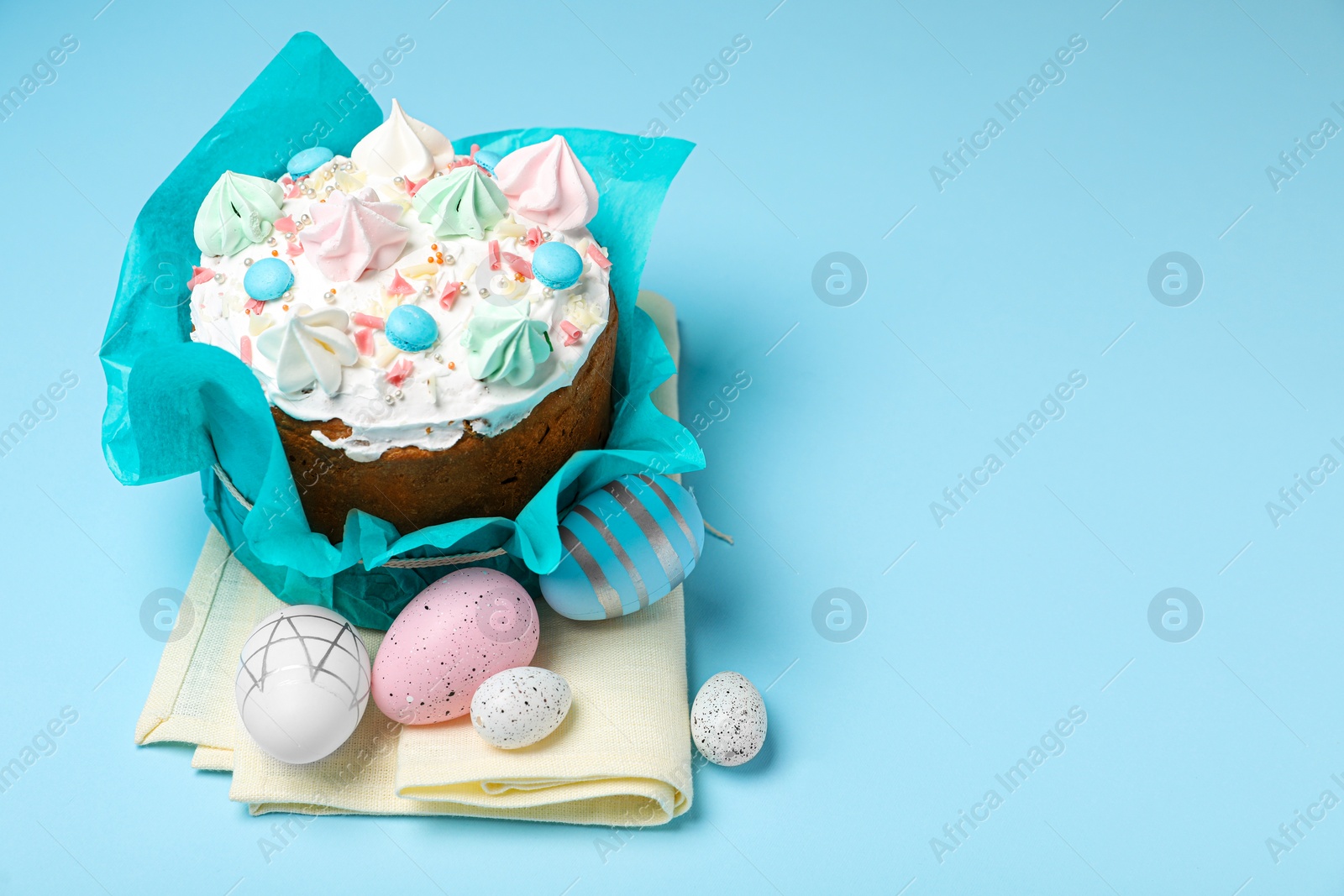 Photo of Traditional Easter cake with meringues and painted eggs on light blue background, space for text