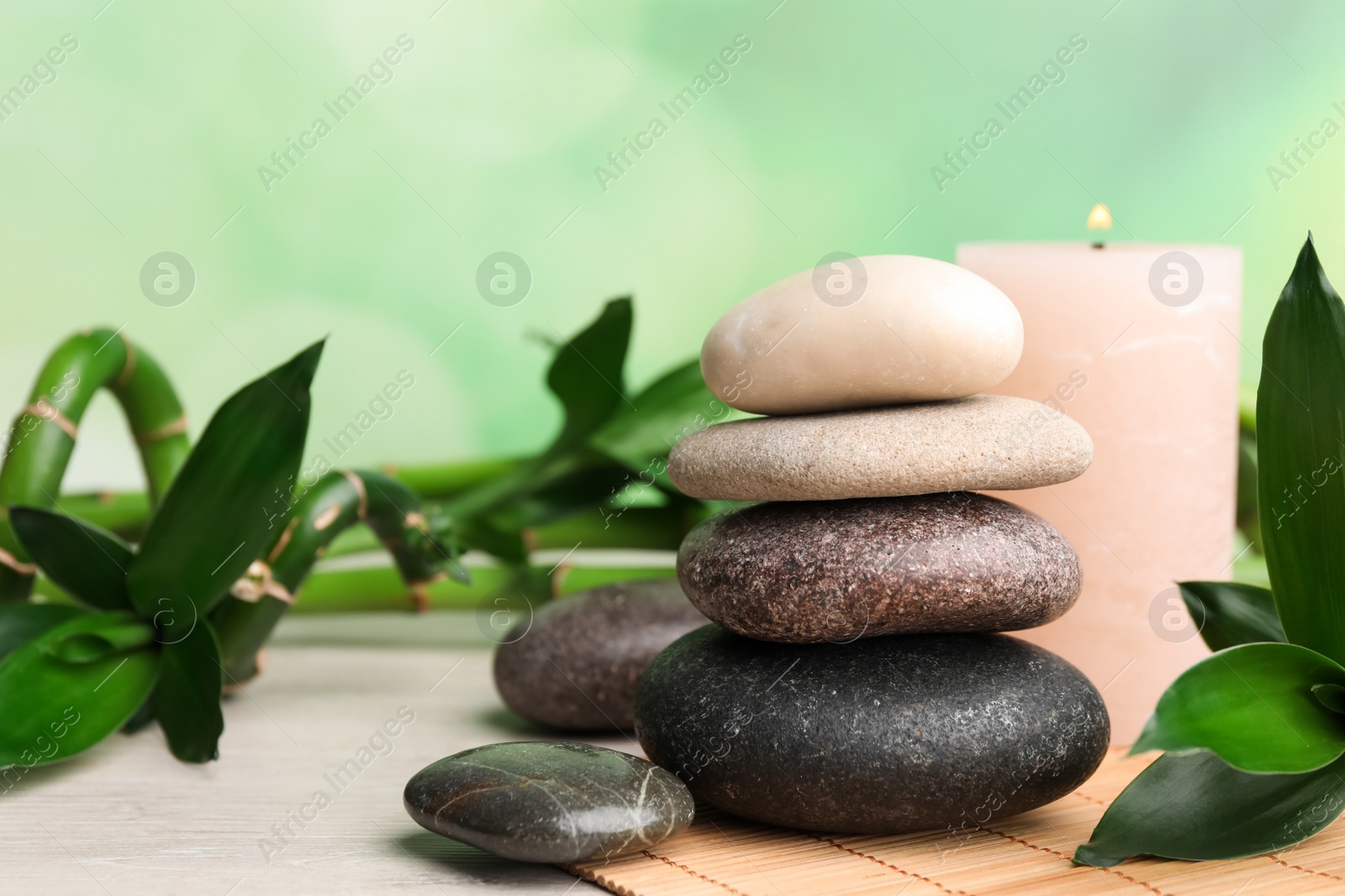 Photo of Stacked spa stones, bamboo and candle on white wooden table. Space for text
