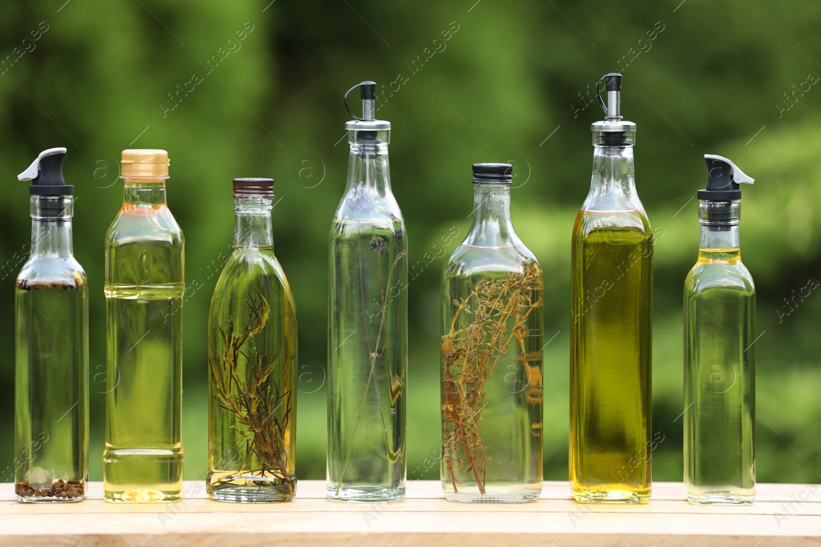 Photo of Many different cooking oils on wooden table against blurred green background