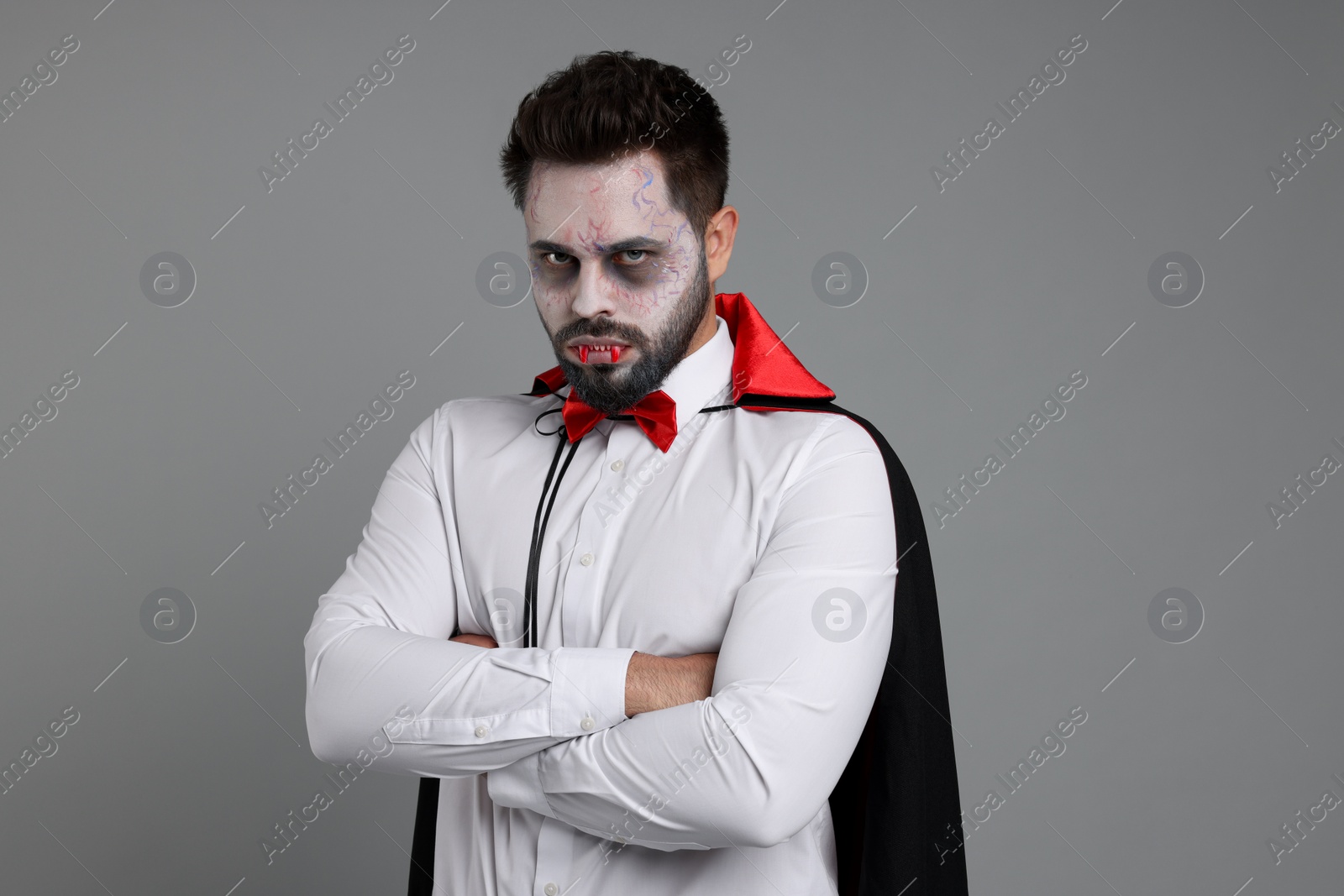 Photo of Man in scary vampire costume with fangs on light grey background. Halloween celebration